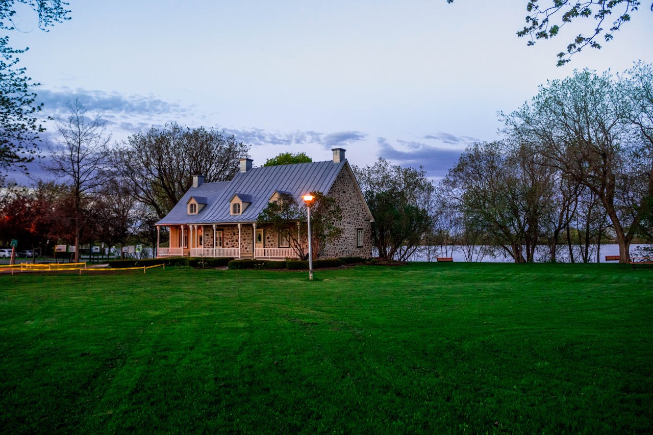 Services Serene stone house by a lakeside with lush green lawn, ideal for real estate and architectural themes.